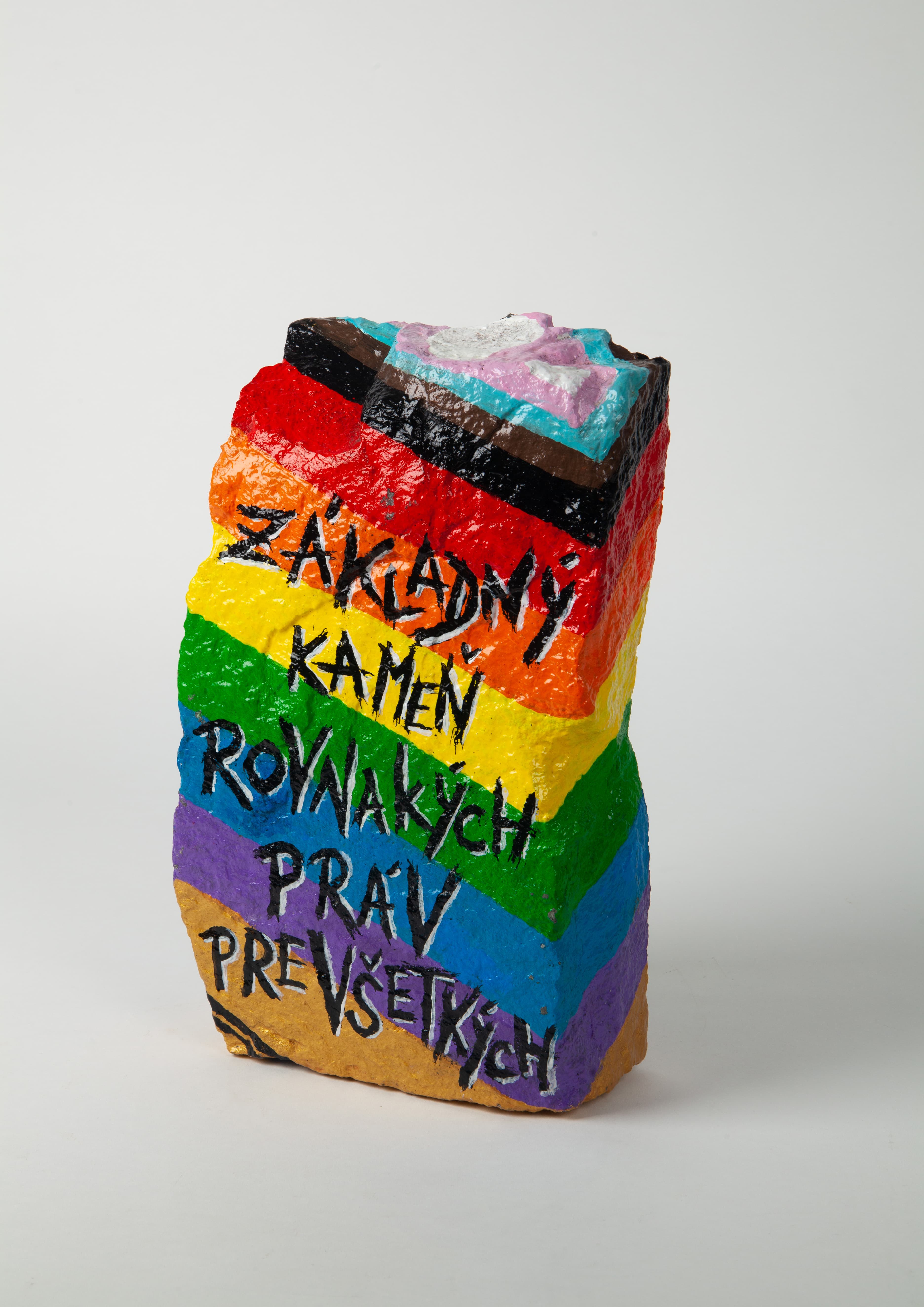 A stone decorated in rainbow colours with text. 